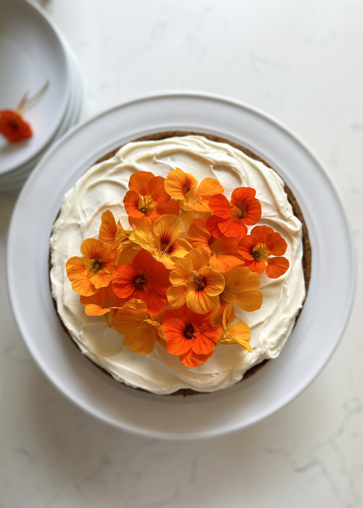 carrot cake single layer with cream cheese frosting and nasturitum flower decor on white cake plate