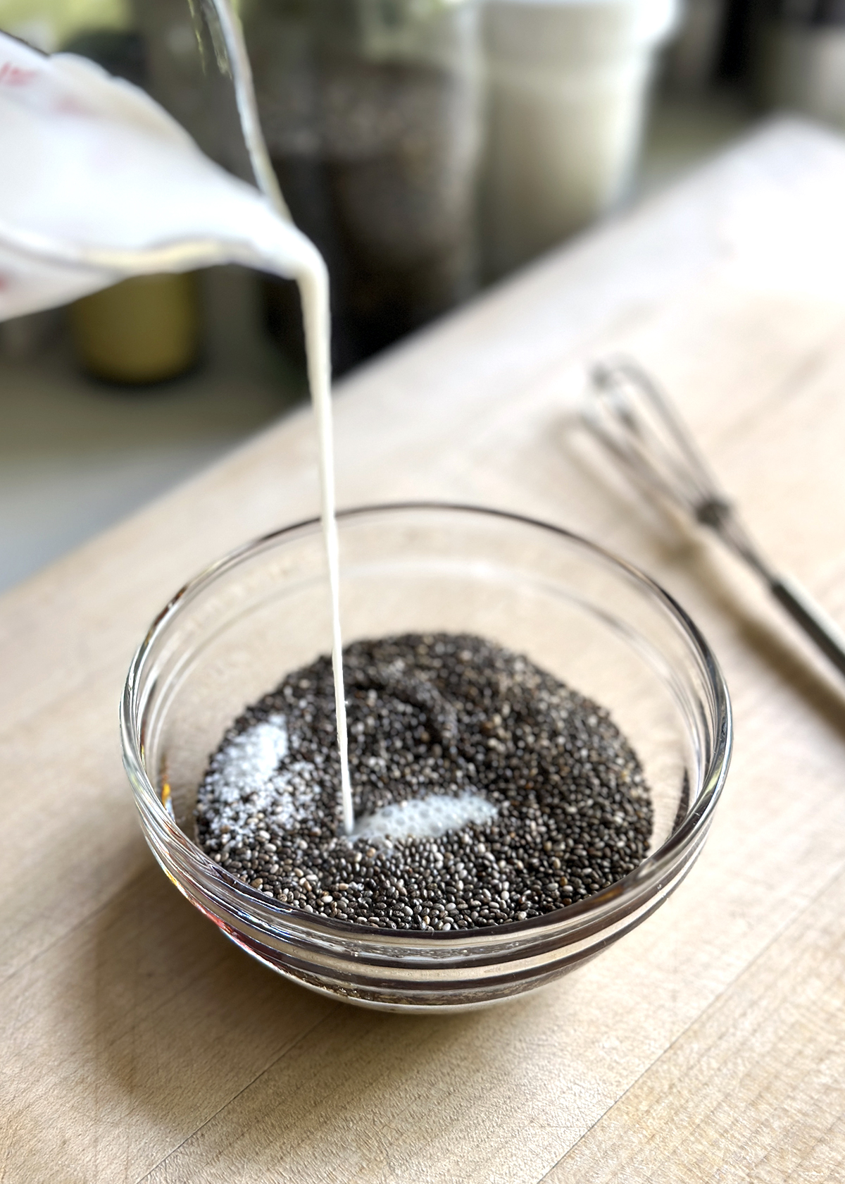 chia seed pudding in glass bowl, milk pouring in