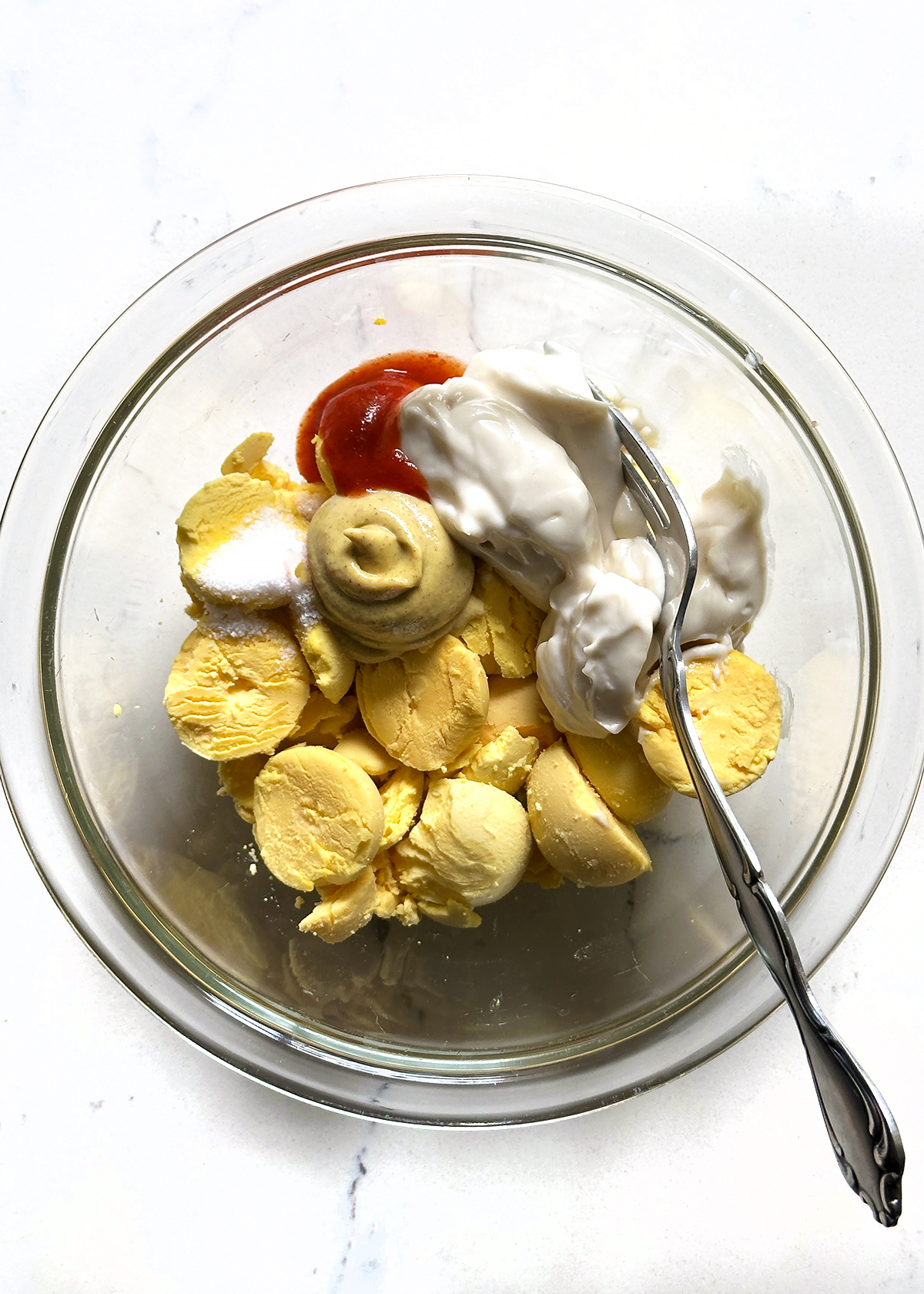 deviled egg yolks mixture in glass bowl with fork
