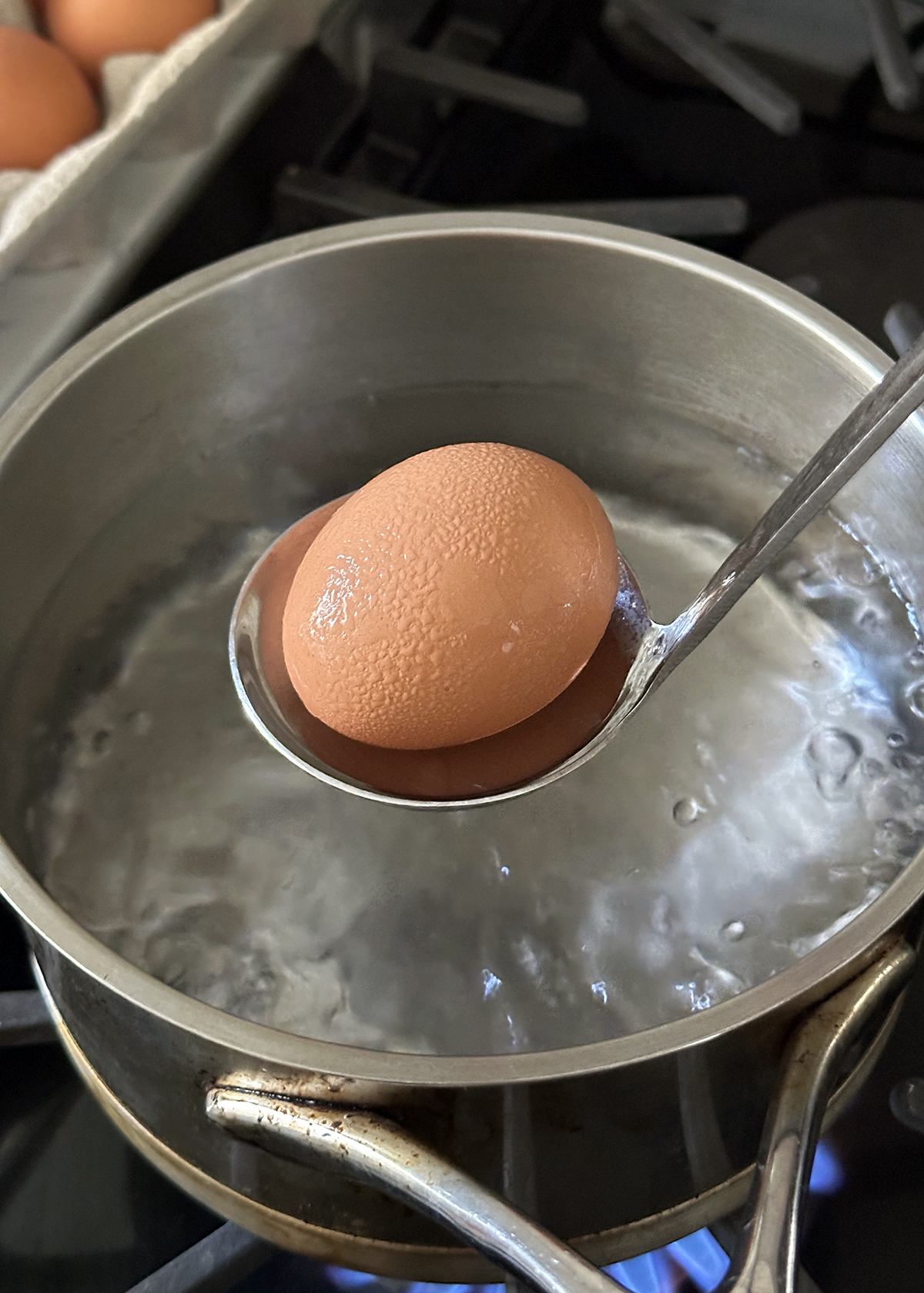 lowering egg in ladle into boiling water