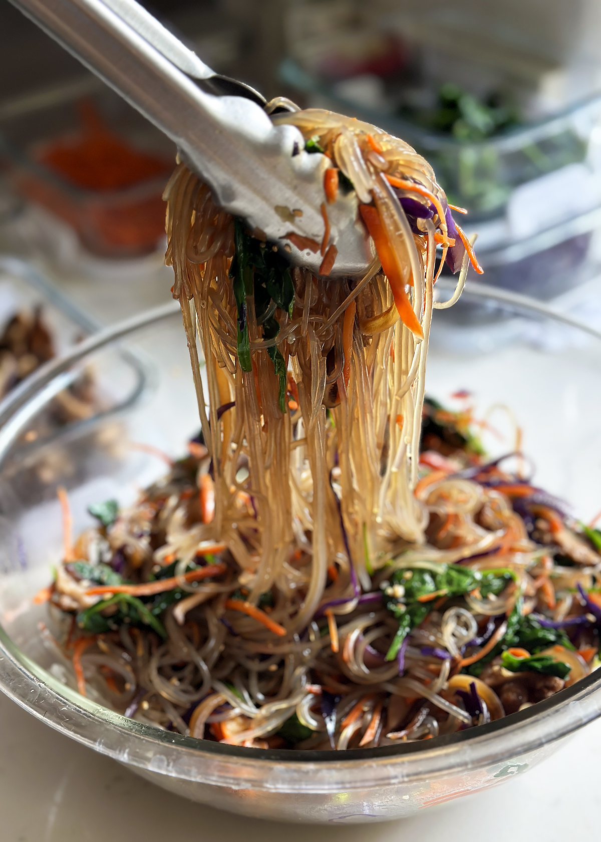 mixing jap chae with sauce with tongs