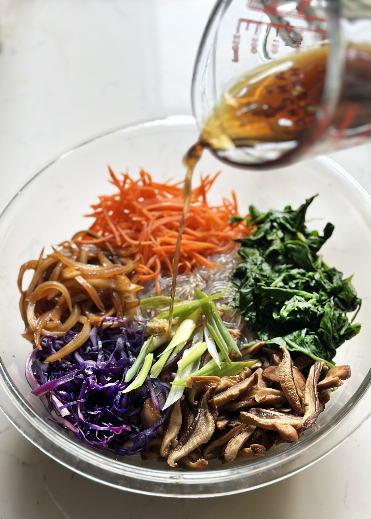 pouring seasoning sauce over jap chae ingredients
