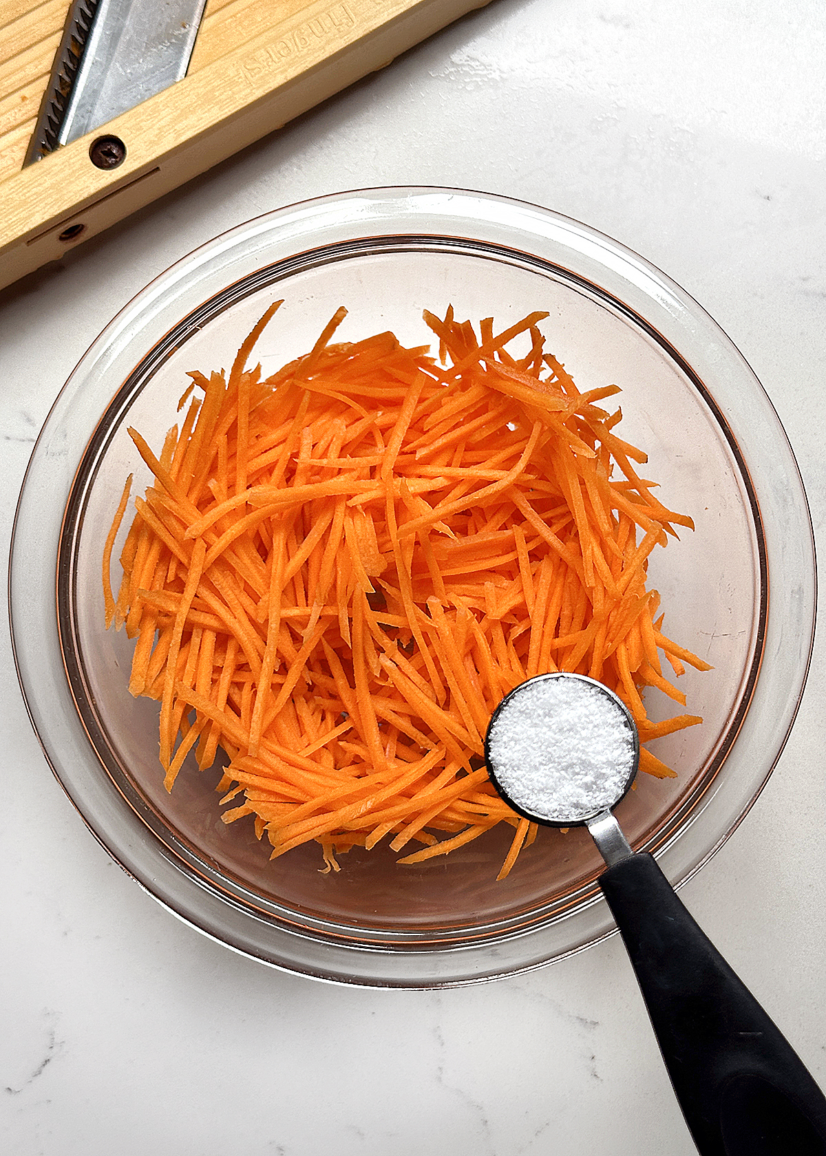 julienned carrots in glass mixing bowl with salt