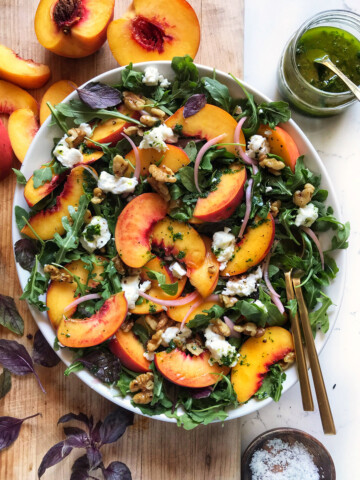 peach arugula salad in white oval bowl on wooden cutting board
